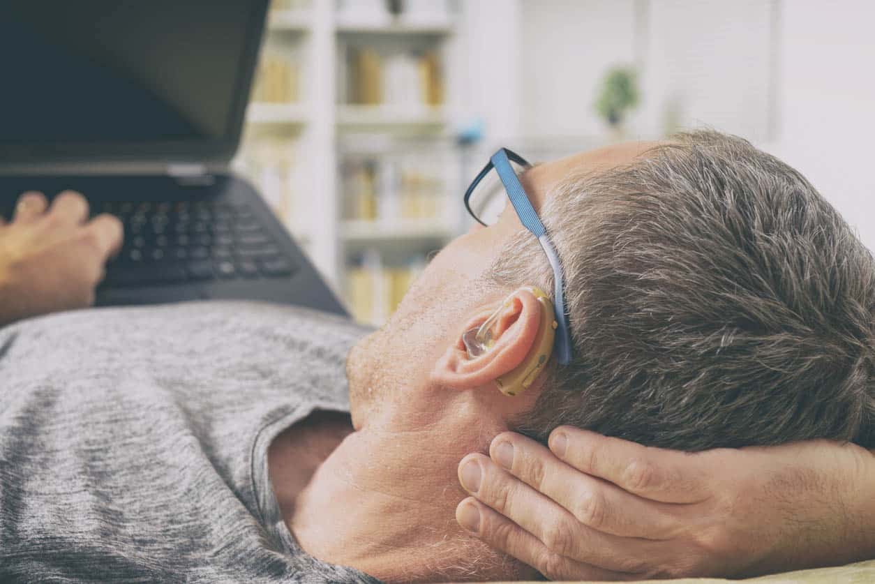 homme équipé d'un appareil auditif devant un ecran ordinateur