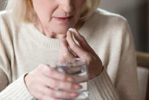 femme mure senior tenant le verre d’eau et un cachet