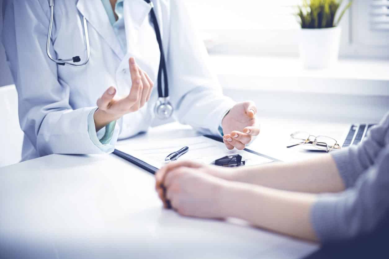 Doctor And Female Patient Sitting At The Desk And Talking In Clinic Near Window. Medicine And Health Care Concept. Green Is Main Color