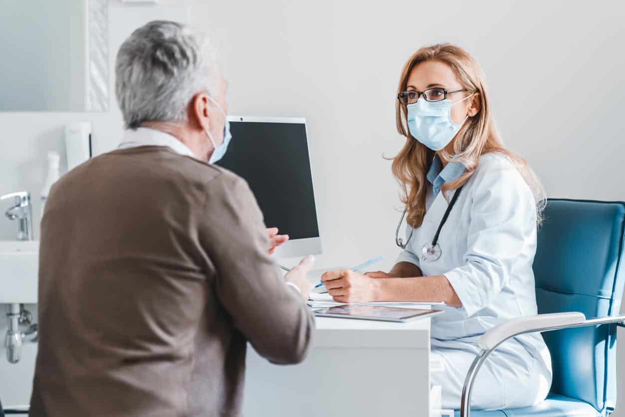 Le docteur de femme portent le masque de visage de protection parlant avec le patient dans le bureau de clinique