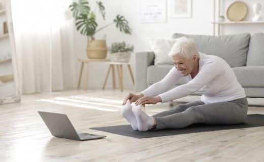 Active Senior Woman Doing Warming Stretching Exercises In Front Of Laptop