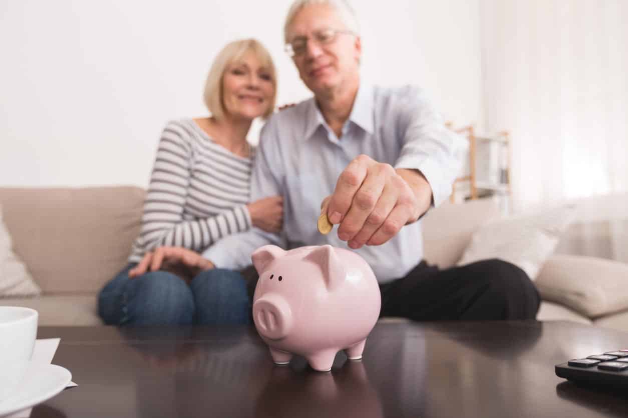 Couple de personnes âgées économiser de l’argent dans sa tirelire à la maison