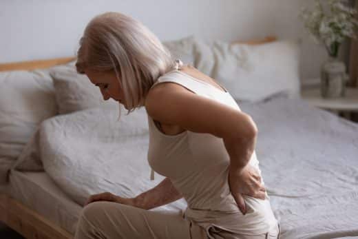 femme assise sur son lit qui a mal au dos