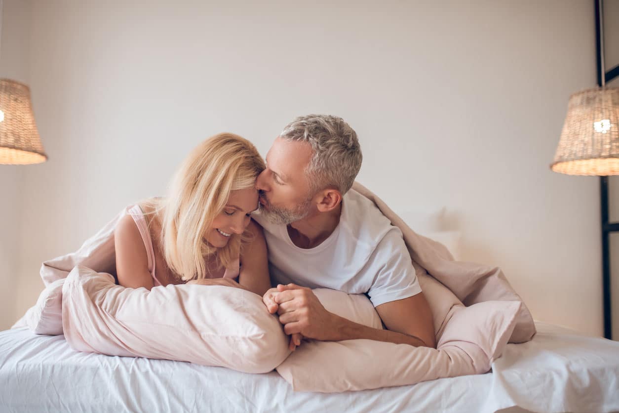 Homme aux cheveux gris et une femme blonde se trouvant sur le lit et se regardant romantique