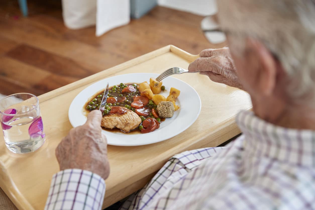 Vue d’épaule du dîner senior homme manger à la maison