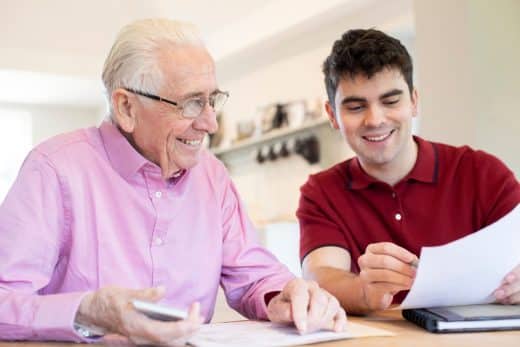 Young Man Helping Senior Neighbor With Paperwork At Home