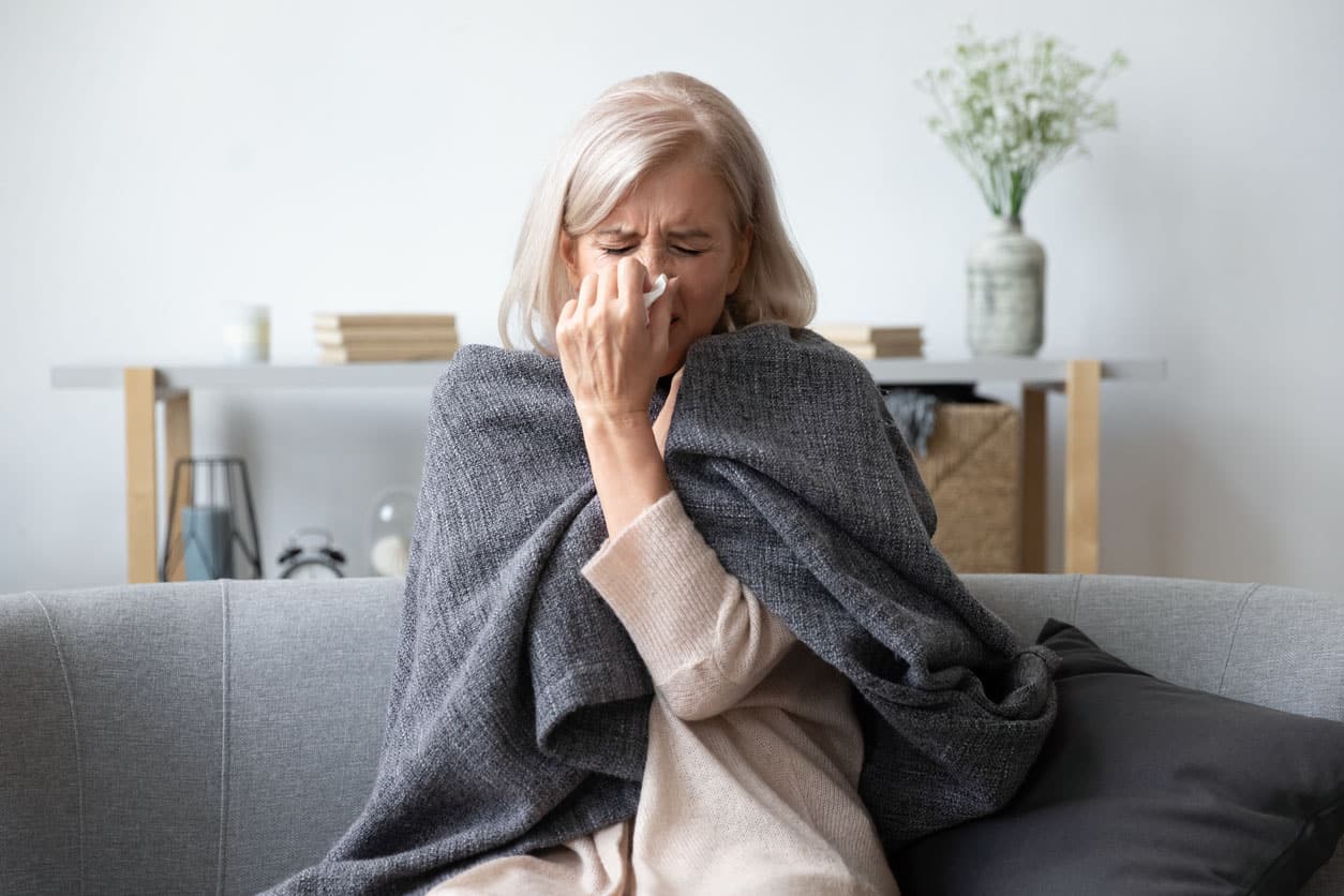 Femme malade âgé éternisant retenant la serviette soufflent le nez coulant  a cause de la grippe