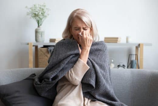 Femme malade âgé éternisant retenant la serviette soufflent le nez coulant a cause d une sinusite chronique