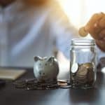 femme mettant des pièces dans un bocal en verre et prenant note avec la tirelire sur la table pour épargner