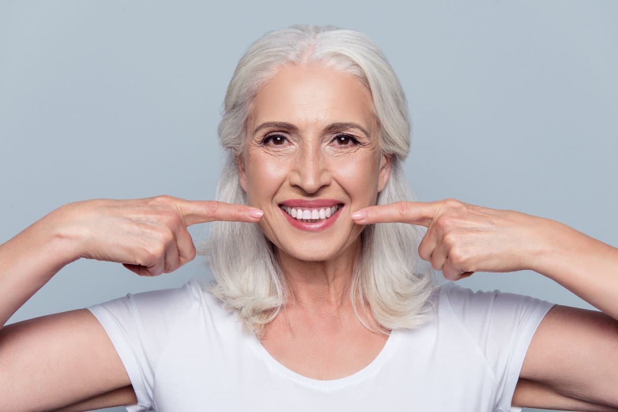 sourire féminin pensionné pointant sur ses dents blanches claire parfaits