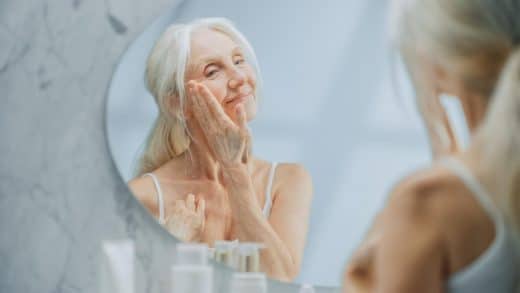 femme âgée, se regardant dans le miroir en appliquant doucement de la crème anti ride pour le visage