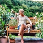 Une Femme Aînée Avec Un Chien Et Un Café S'asseyant à L'extérieur Sur Une Terrasse De Maison En été