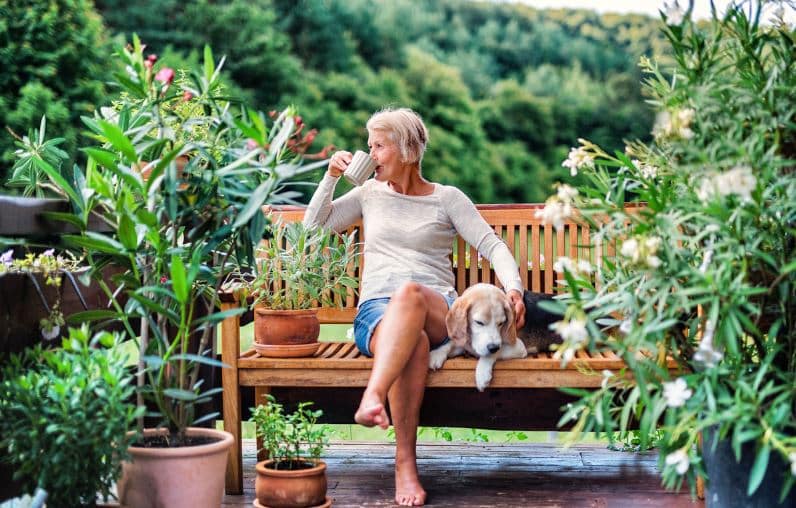 Une Femme Aînée Avec Un Chien Et Un Café S'asseyant à L'extérieur Sur Une Terrasse De Maison En été