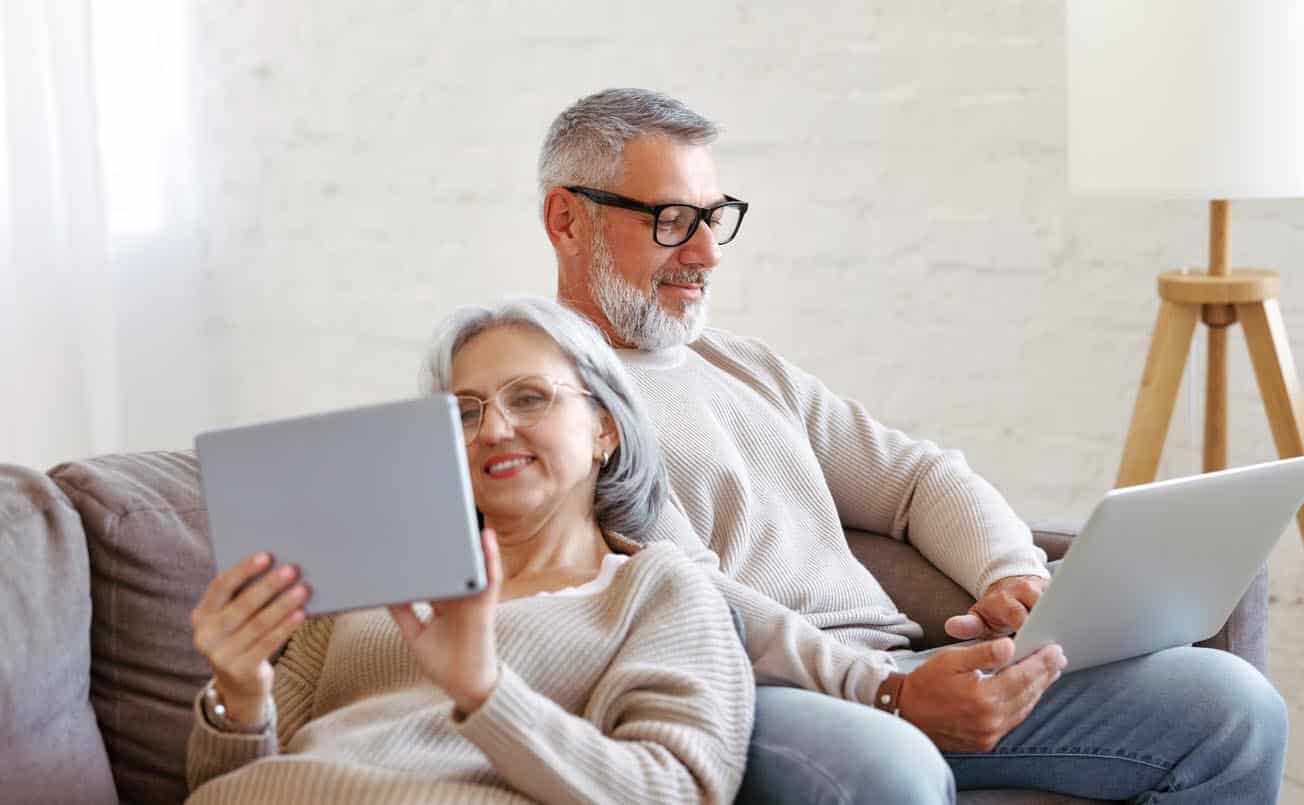 couple familial à la retraite utilisant des technologies modernes ordinateur portable et tablette numérique à la maison pour comparer les lunettes