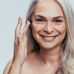 Femme Mure Qui Se Met De La Creme Sur Le Visage En Souriant